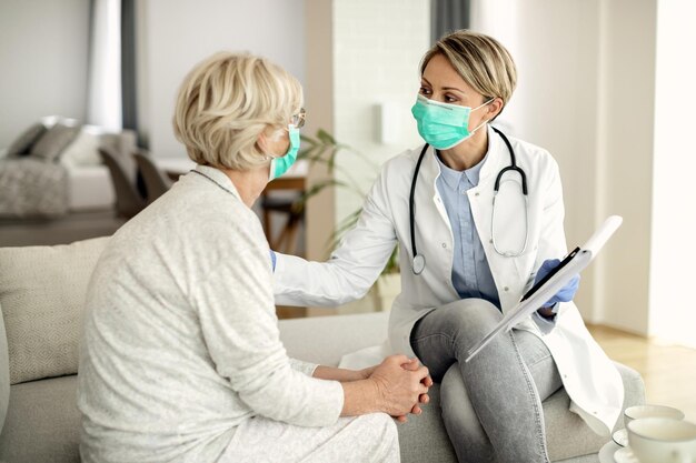 Doctora hablando con una mujer madura mientras la visitaba en casa durante la epidemia de coronavirus