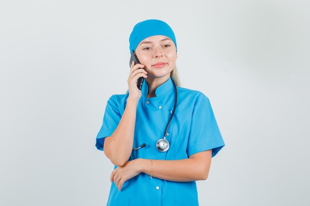 Doctora hablando por teléfono móvil y sonriendo en uniforme azul