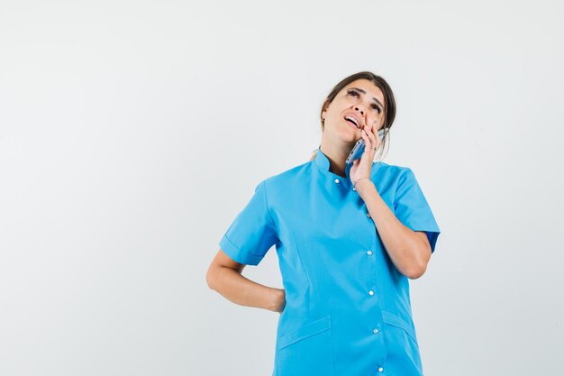 Doctora hablando por teléfono móvil en uniforme azul y mirando pensativo
