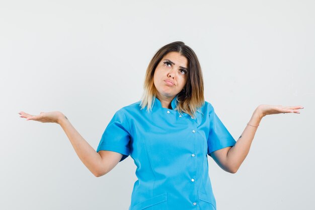 Doctora haciendo gesto de escalas en uniforme azul y mirando confundido