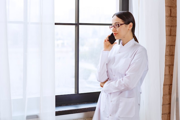 Doctora con una importante llamada telefónica cerca de la ventana.