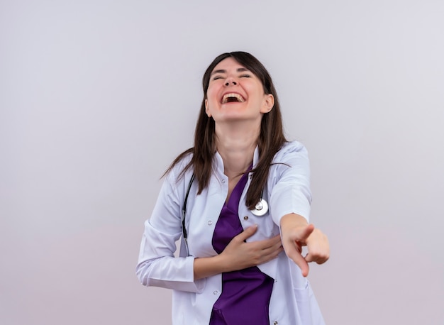 Doctora joven alegre en bata médica con puntos de estetoscopio en la cámara sobre fondo blanco aislado con espacio de copia