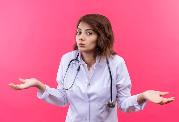 Foto gratuita doctora joven en bata blanca con estetoscopio mirando incierto y confundido encogiéndose de hombros sin respuesta