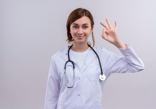 Doctora joven complacida con bata médica y un estetoscopio haciendo bien firmar con espacio de copia