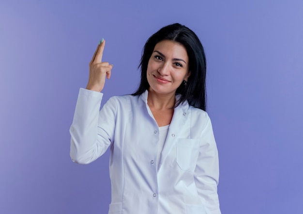 Doctora joven complacida vistiendo bata médica mirando hacia arriba