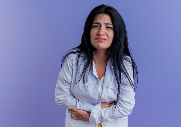 Doctora joven dolorido vistiendo bata médica mirando sosteniendo el vientre