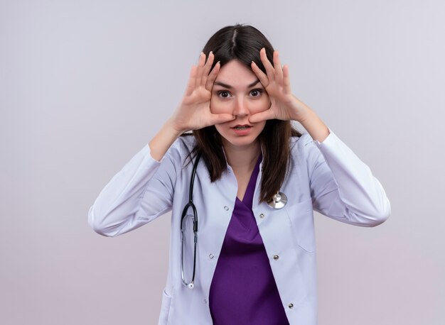 Doctora joven molesta en bata médica con estetoscopio pone la mano en la cara sobre fondo blanco aislado con espacio de copia