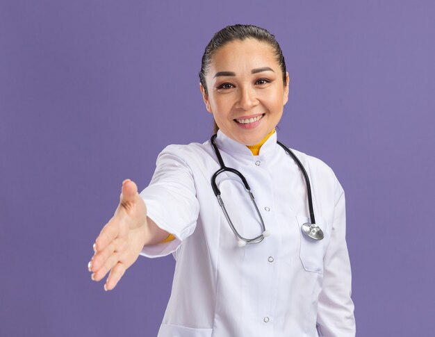 Foto gratuita doctora joven con sonrisa en la cara ofreciendo saludo de mano