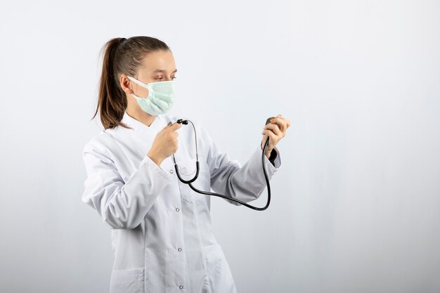 Doctora joven en uniforme blanco mirando un estetoscopio