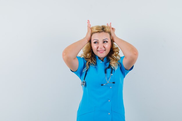 Doctora juntando la cabeza con las manos en uniforme azul y mirando feliz.
