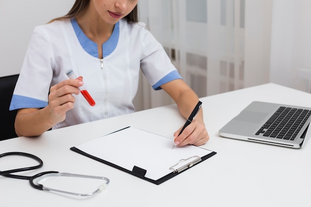 Doctora mano escribiendo un informe y sosteniendo una muestra de sangre