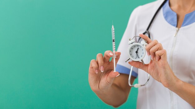 Doctora manos sosteniendo una jeringa y un reloj