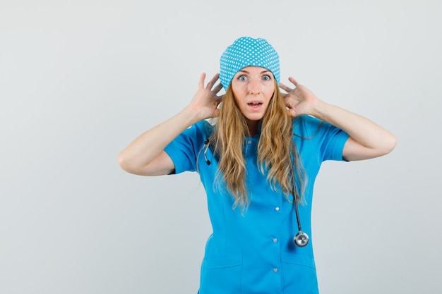 Doctora manteniendo las manos cerca de las orejas en uniforme azul y mirando ansiosa