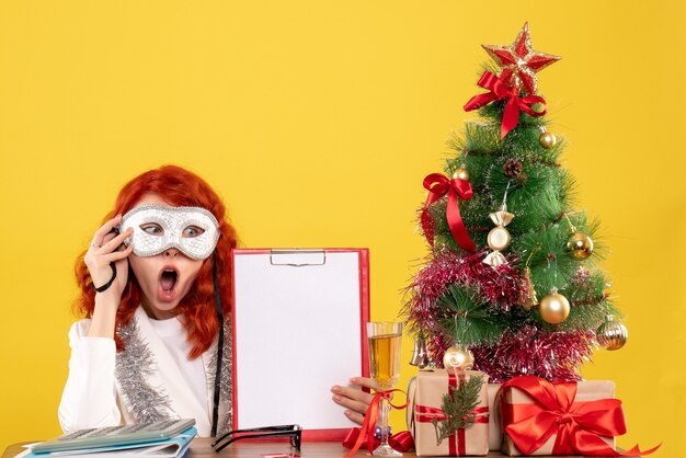 Doctora con máscara alrededor del árbol de Navidad y regalos en amarillo