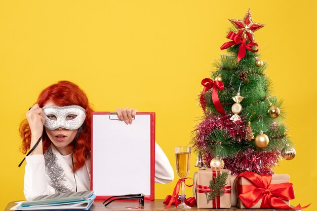 Doctora con máscara alrededor del árbol de Navidad y regalos en amarillo