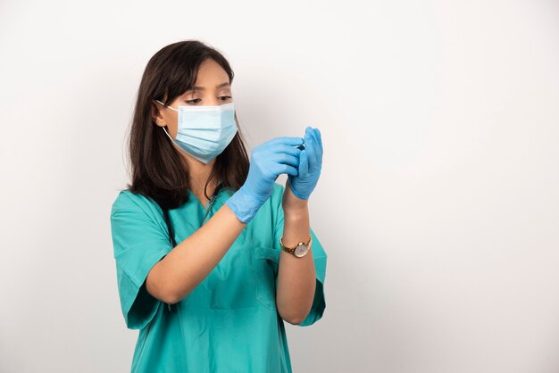 Doctora con máscara médica mirando un par de guantes sobre fondo blanco. Foto de alta calidad