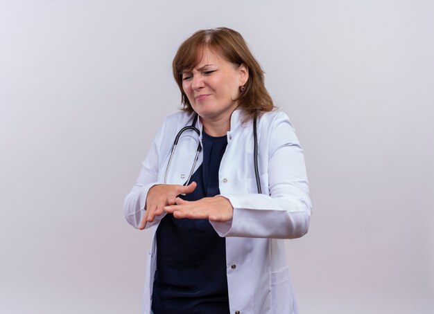 Doctora de mediana edad disgustada vistiendo bata médica y estetoscopio levantando las manos sobre fondo blanco aislado con espacio de copia