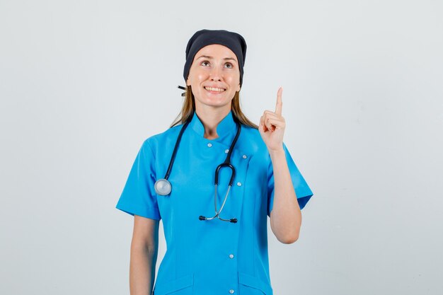 Doctora mirando hacia arriba con el dedo firme en uniforme y mirando alegre. vista frontal.