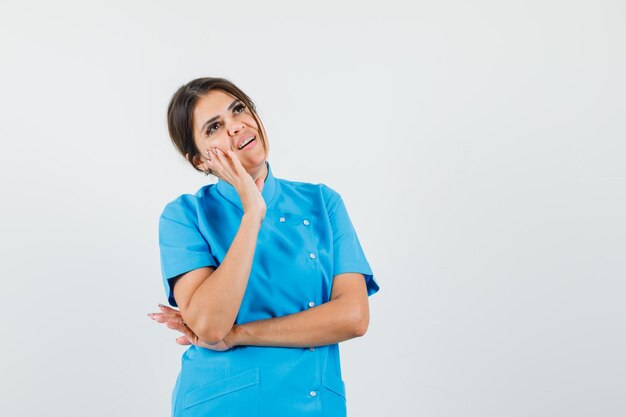 Doctora mirando hacia arriba en uniforme azul y mirando soñadora