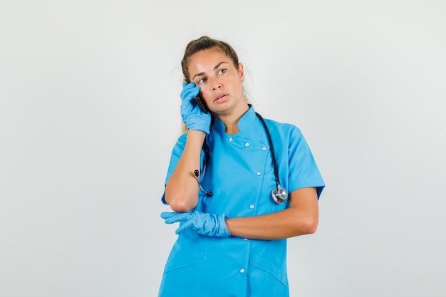 Doctora mirando a un lado mientras habla por teléfono inteligente en uniforme azul