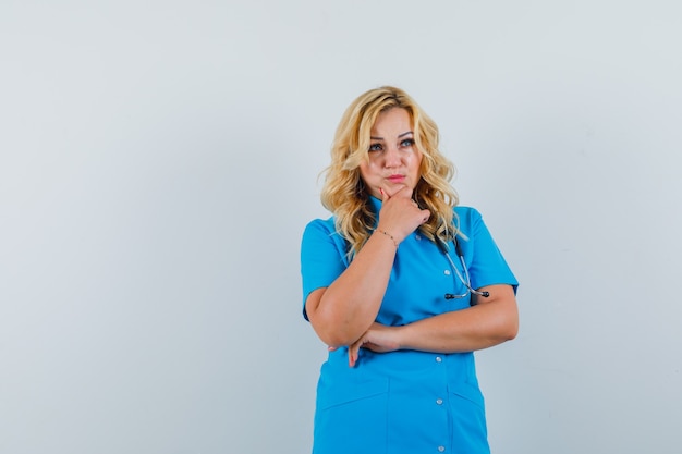 Doctora mirando a otro lado con la mano en la mandíbula en uniforme azul y mirando pensativo. espacio para texto