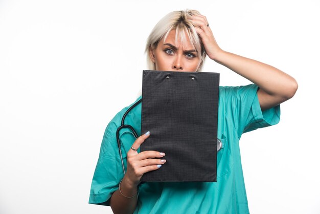 Doctora mirando portapapeles sobre fondo blanco sosteniendo su cabello. Foto de alta calidad