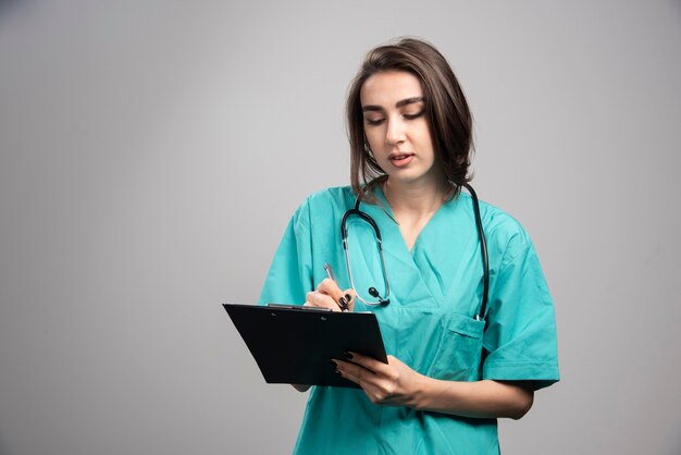 Doctora mirando portapapeles sobre fondo gris. Foto de alta calidad