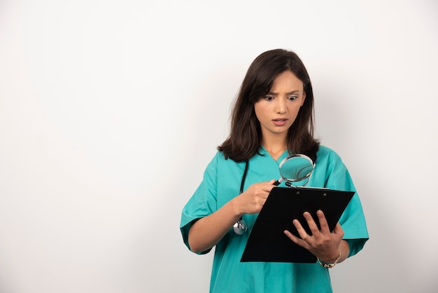 Doctora mirando resultados con lupa sobre fondo blanco.