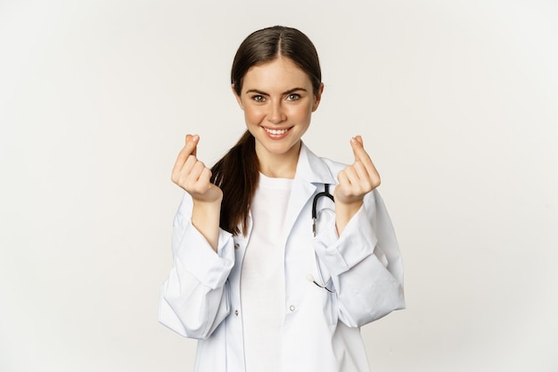 Doctora mostrando corazones de dedo sonriendo con cuidado de pie en uniforme sobre fondo blanco.