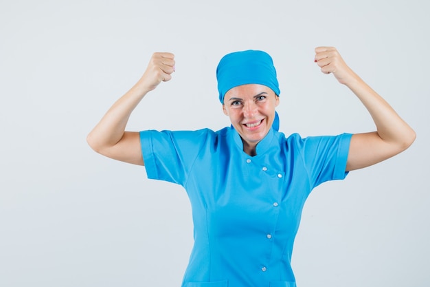 Doctora mostrando gesto ganador en uniforme azul y luciendo dichoso. vista frontal.