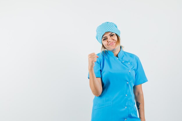 Doctora mostrando gesto ganador en uniforme azul y mirando feliz