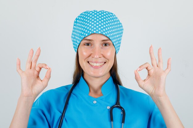 Doctora mostrando gesto ok en uniforme azul y con aspecto alegre. vista frontal.