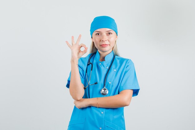 Doctora mostrando gesto ok en uniforme azul y mirando complacido