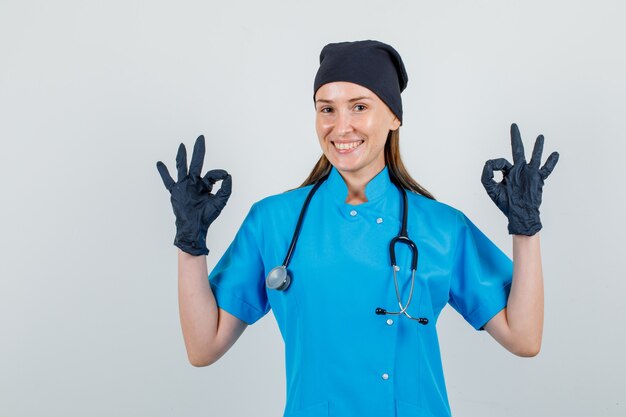 Doctora mostrando gesto ok en uniforme, guantes y mirando alegre