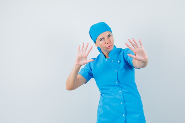 Doctora mostrando gesto de parada para calmarse en vista frontal uniforme azul.