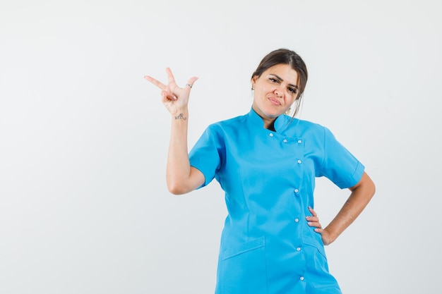 Doctora mostrando gesto de 'te amo' en uniforme azul y mirando confiado