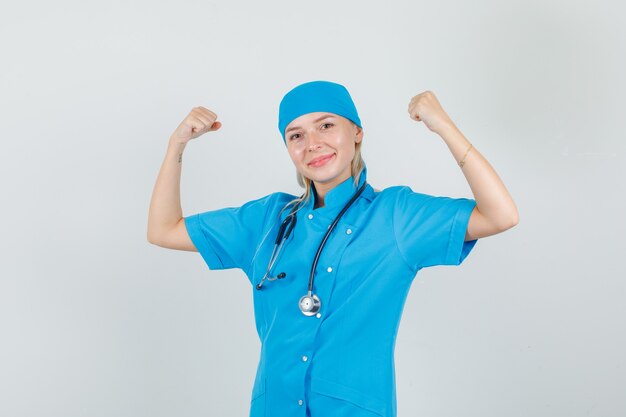 Doctora mostrando músculos y sonriendo en uniforme azul y luciendo fuerte.