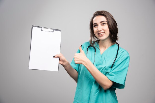 Doctora mostrando portapapeles sobre fondo gris. Foto de alta calidad