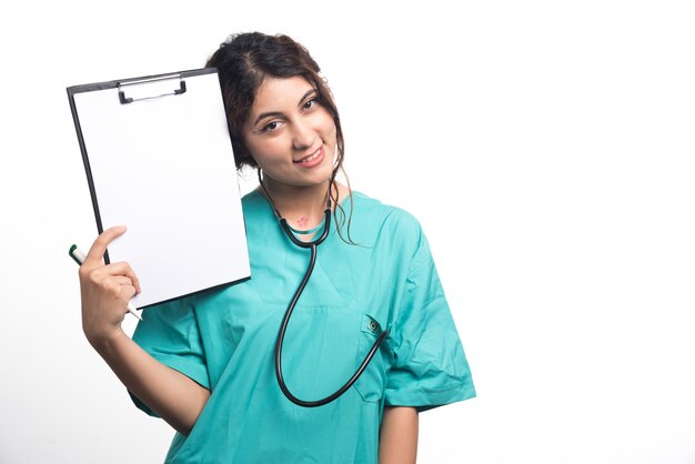 Doctora mostrando portapapeles vacío con lápiz y estetoscopio sobre fondo blanco. Foto de alta calidad