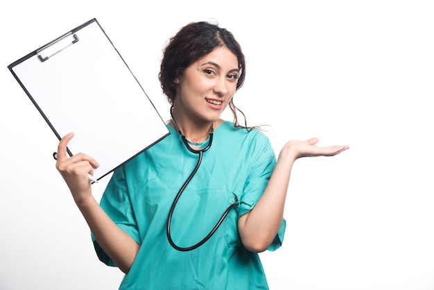 Doctora mostrando portapapeles vacío con lápiz y estetoscopio sobre fondo blanco. Foto de alta calidad
