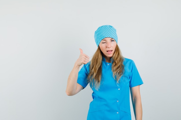 Foto gratuita doctora mostrando el pulgar hacia arriba y guiñando el ojo en uniforme azul