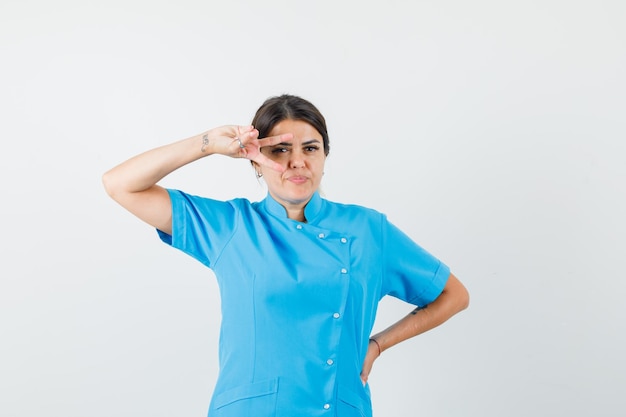 Doctora mostrando el signo de la victoria en el ojo en uniforme azul y mirando confiado