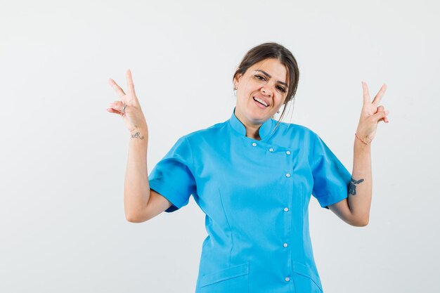 Doctora mostrando el signo de la victoria en uniforme azul y mirando feliz