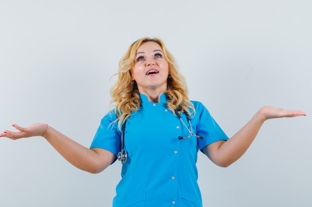 Doctora mostrando sus emociones con las manos arriba en uniforme azul y mirando deseosa.