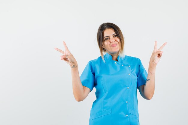 Doctora mostrando v-sign en uniforme azul y mirando feliz