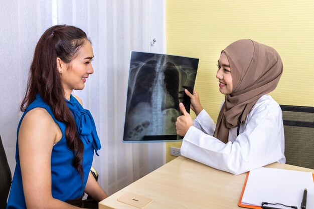 Una doctora musulmana examinando y mirando apuntando a una película de rayos X dando una explicación al paciente que está sentado en una silla