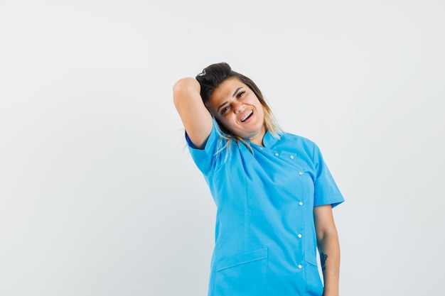 Doctora posando mientras mantiene levantada la mano sobre la cabeza en uniforme azul