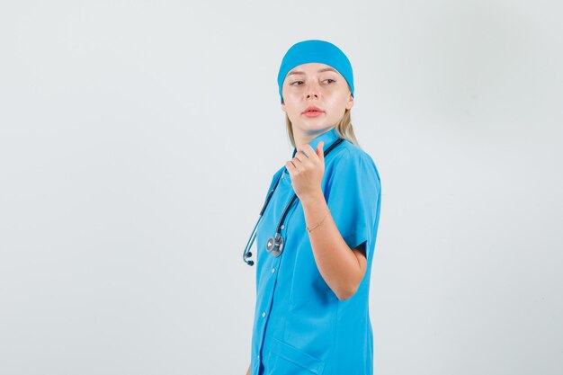 Doctora posando mientras mira por encima del hombro en uniforme azul y se ve estricta.