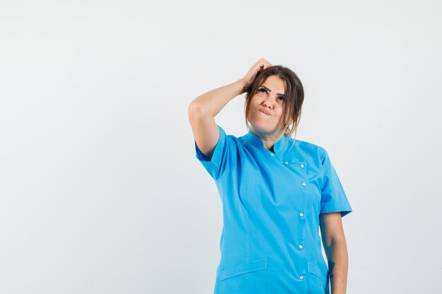 Doctora rascándose la cabeza en uniforme azul y mirando soñadora