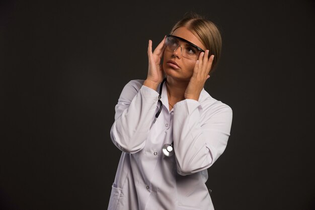 Doctora rubia con un estetoscopio usando anteojos y mirando hacia arriba.